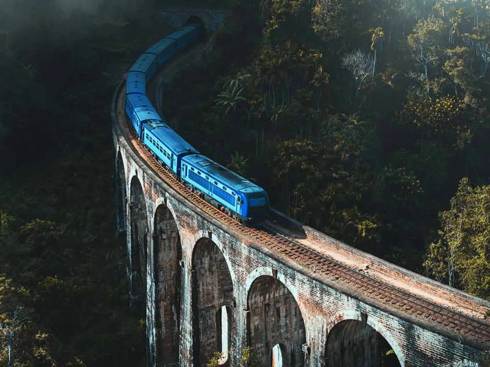 A blue train crossing the historic Nine Arch Bridge through the jungle near Ella