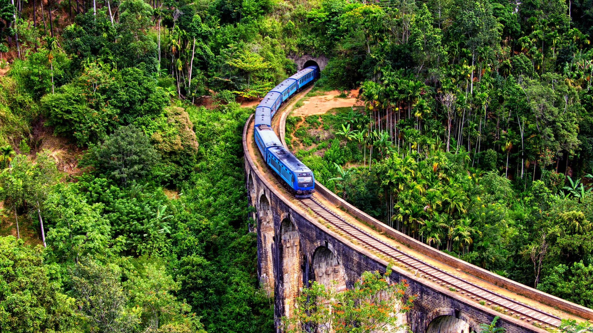 A blue train crossing the Nine Arch Bridge through misty hills near Ella