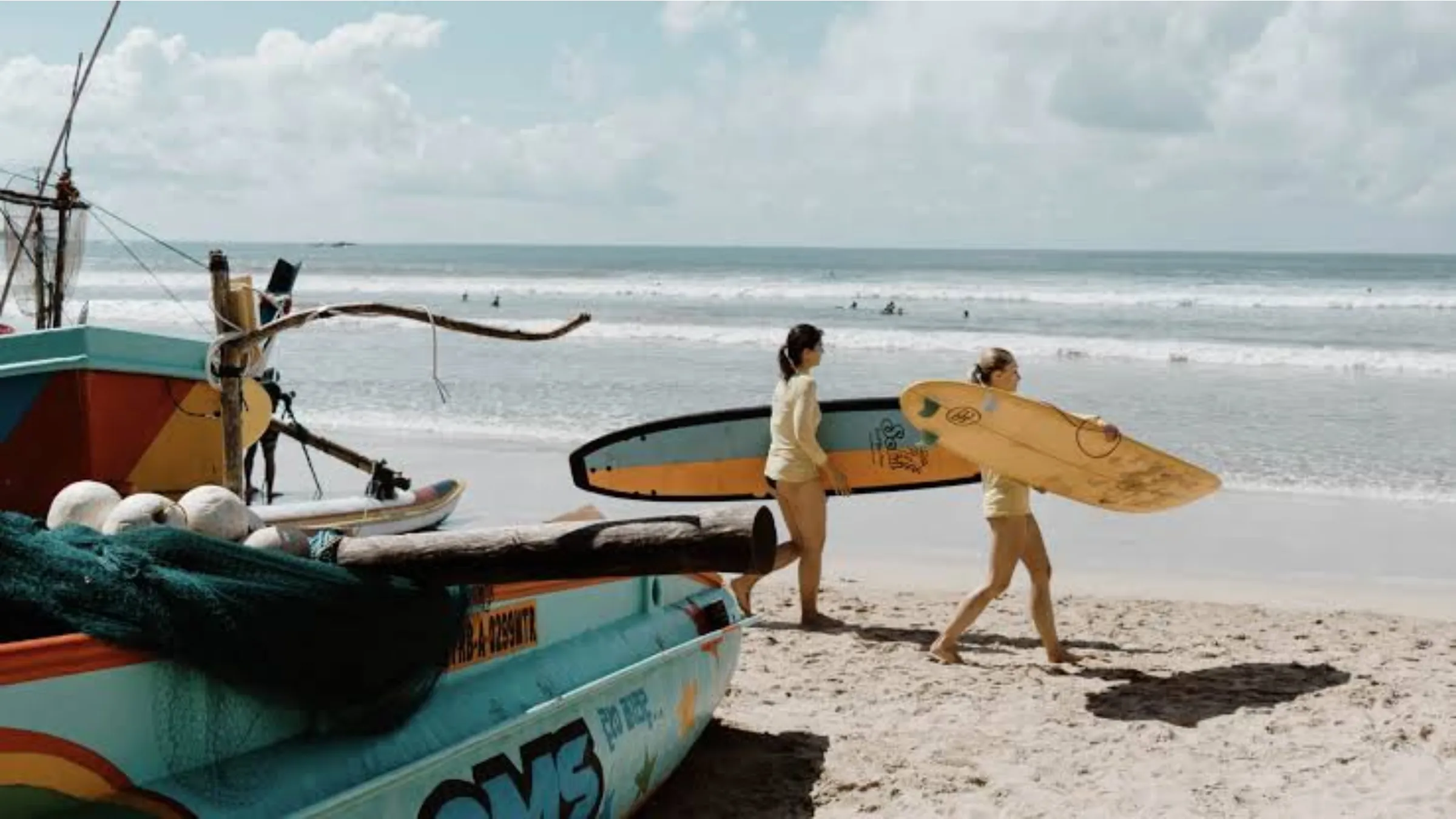 Surfers carrying boards past a traditional fishing boat on a Sri Lankan beach