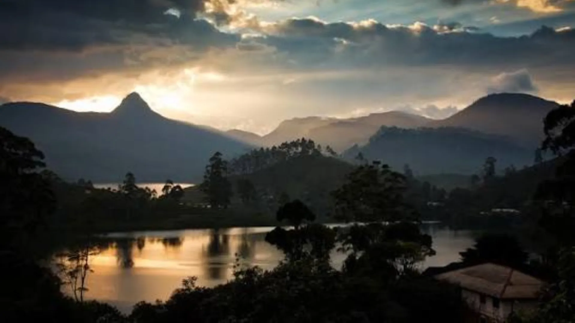 Mountain peaks silhouetted against a golden sunset sky above a still lake in Sri Lanka's hill country