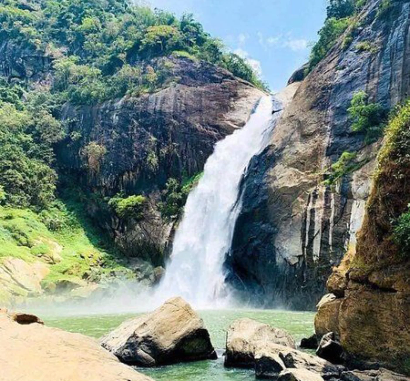A tall waterfall plunging down a rocky gorge into a green pool, surrounded by forest